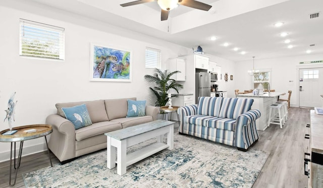 living room featuring ceiling fan with notable chandelier and light hardwood / wood-style floors