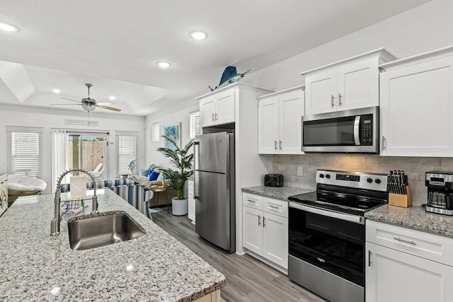 kitchen with white cabinets, appliances with stainless steel finishes, sink, backsplash, and ceiling fan