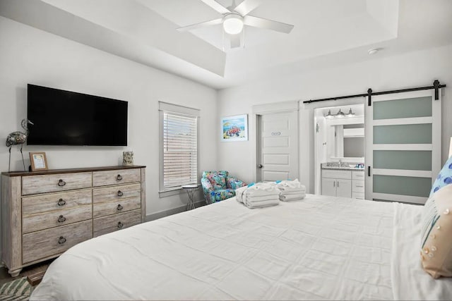 bedroom with a tray ceiling, sink, ceiling fan, ensuite bathroom, and a barn door