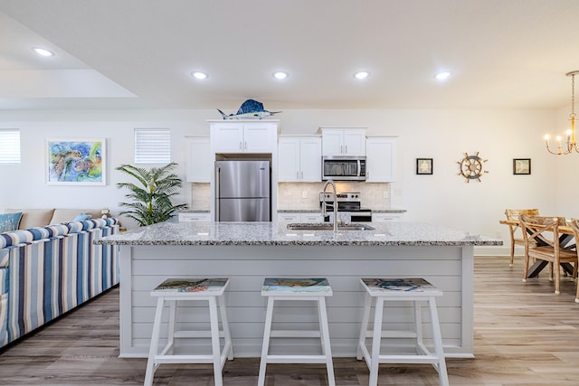 kitchen featuring white cabinets, an island with sink, stainless steel appliances, and hardwood / wood-style flooring