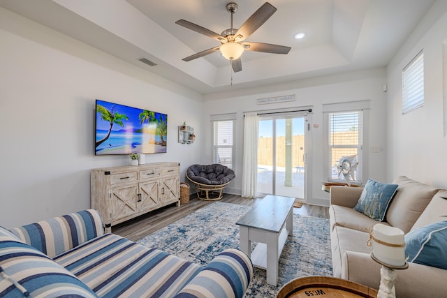 living room featuring hardwood / wood-style flooring, ceiling fan, and a raised ceiling