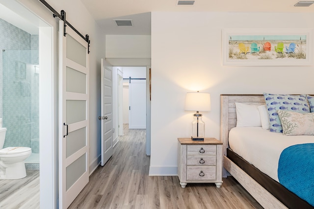 bedroom featuring ensuite bath, a barn door, and light wood-type flooring