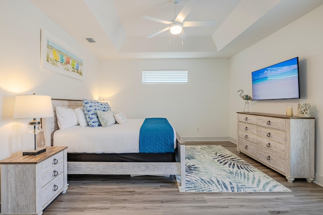 bedroom with ceiling fan, light hardwood / wood-style flooring, and a raised ceiling