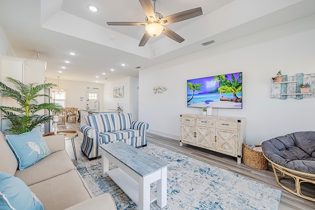 living room with ceiling fan, sink, a tray ceiling, and hardwood / wood-style flooring