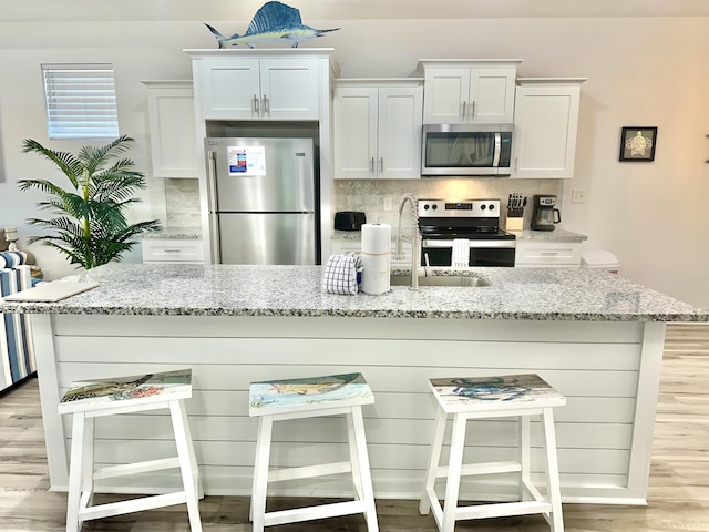 21400 Marlin Ave, Panama City Beach, FL 32413 - kitchen with an island with sink, a breakfast bar area, white cabinetry, stainless steel appliances, and decorative backsplash