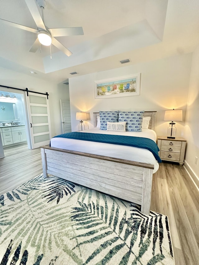 21400 Marlin Ave, Panama City Beach, FL 32413 - bedroom with light wood-type flooring, a raised ceiling, a barn door, ceiling fan, and visible vents