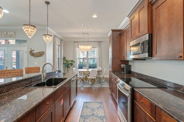 kitchen featuring sink, hanging light fixtures, dark stone counters, appliances with stainless steel finishes, and ornamental molding