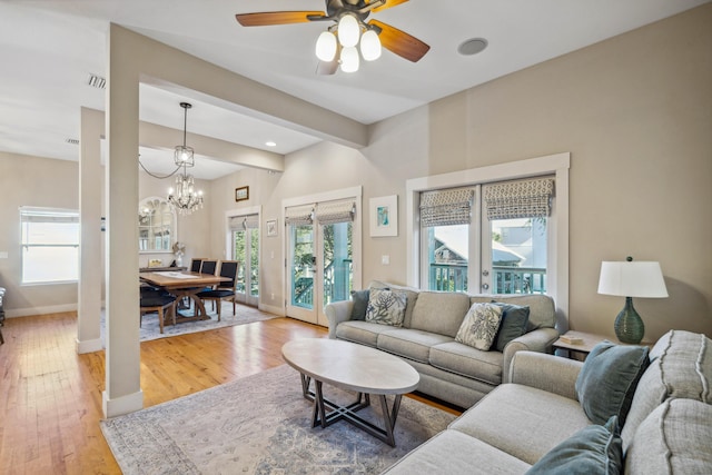 living room featuring ceiling fan with notable chandelier, hardwood / wood-style flooring, beam ceiling, and french doors