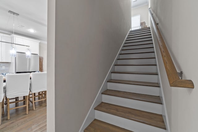 staircase featuring wood-type flooring, an inviting chandelier, and ornamental molding