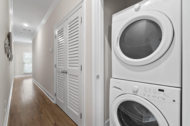 clothes washing area with stacked washer / drying machine, crown molding, and dark wood-type flooring