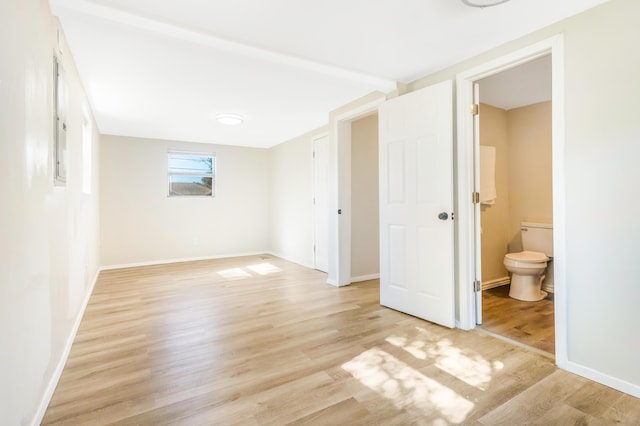 unfurnished bedroom featuring light wood finished floors, connected bathroom, and baseboards