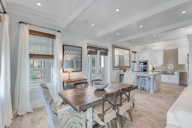 dining room featuring beamed ceiling, light hardwood / wood-style flooring, and a healthy amount of sunlight