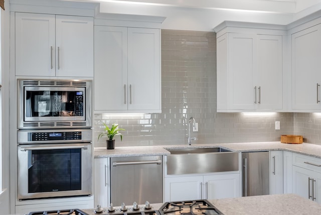 kitchen with light stone countertops, appliances with stainless steel finishes, backsplash, sink, and white cabinetry