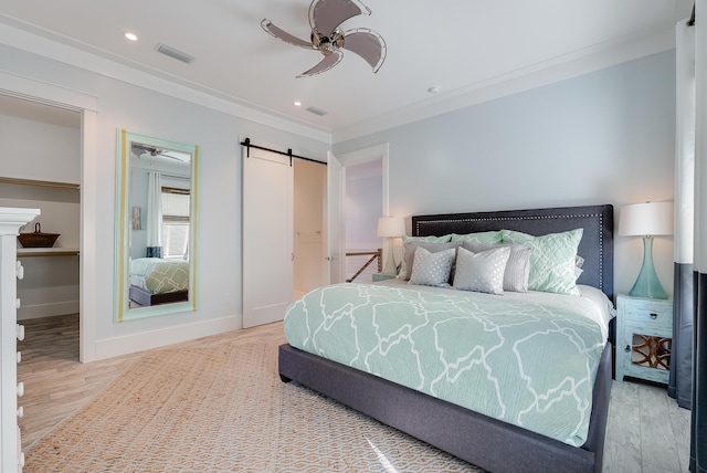 bedroom with ceiling fan, a barn door, light wood-type flooring, and crown molding