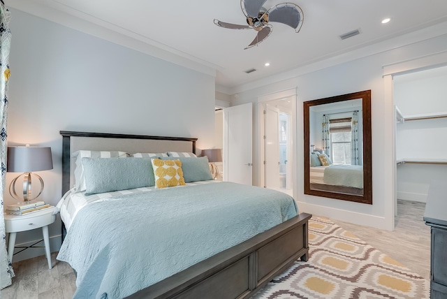 bedroom with light hardwood / wood-style floors, a spacious closet, ceiling fan, and ornamental molding