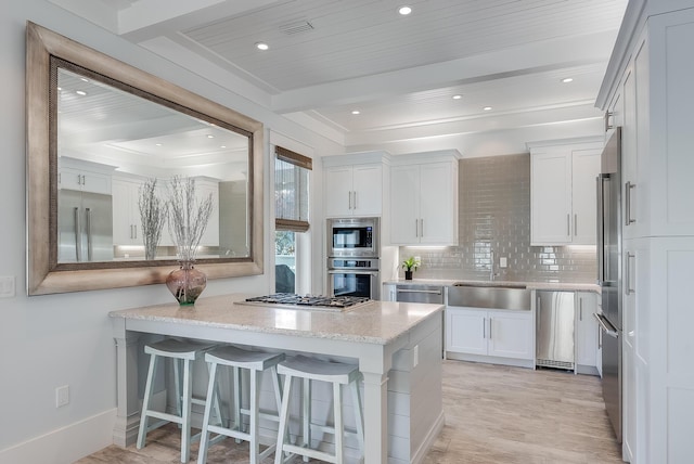 kitchen with sink, built in appliances, a kitchen bar, decorative backsplash, and white cabinets