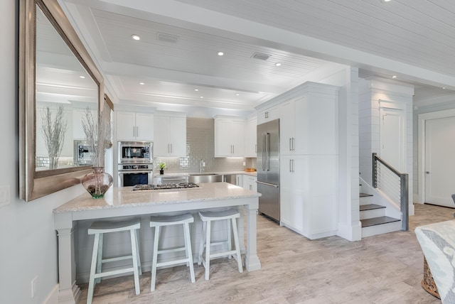 kitchen featuring light stone countertops, a kitchen breakfast bar, built in appliances, beamed ceiling, and white cabinetry