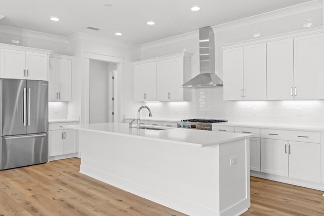 kitchen featuring wall chimney exhaust hood, a kitchen island with sink, sink, white cabinetry, and stainless steel refrigerator