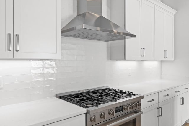 kitchen featuring decorative backsplash, stainless steel range, white cabinets, and wall chimney range hood