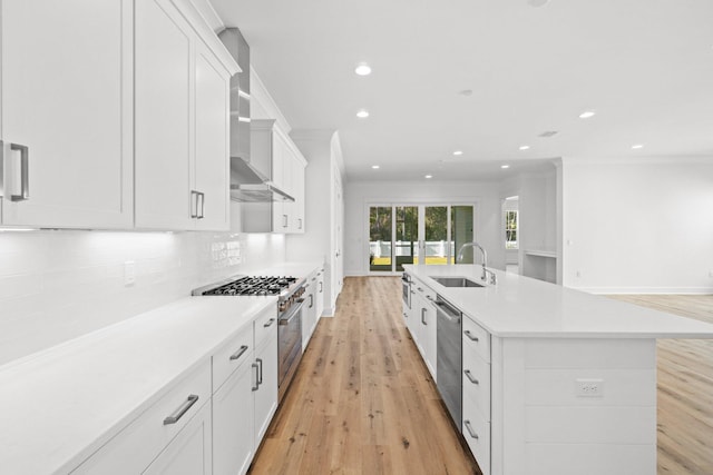 kitchen with a kitchen island with sink, sink, white cabinets, and wall chimney range hood