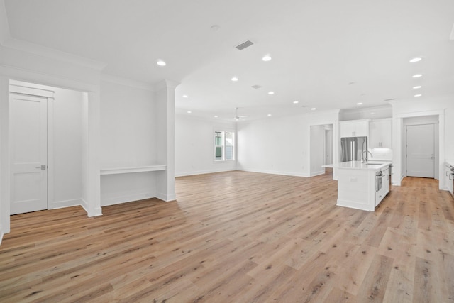 unfurnished living room with light hardwood / wood-style flooring, ceiling fan, crown molding, and sink