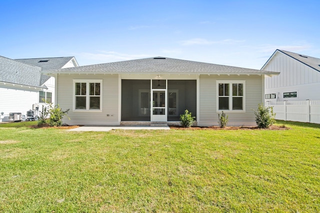 back of property featuring roof with shingles, a lawn, fence, and a sunroom