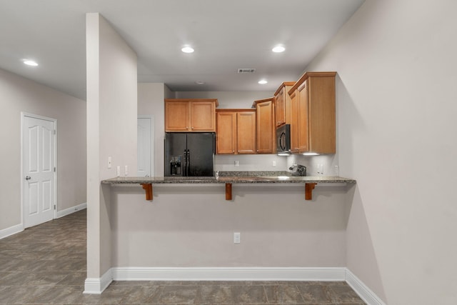 kitchen featuring a kitchen breakfast bar, black appliances, kitchen peninsula, and dark stone counters