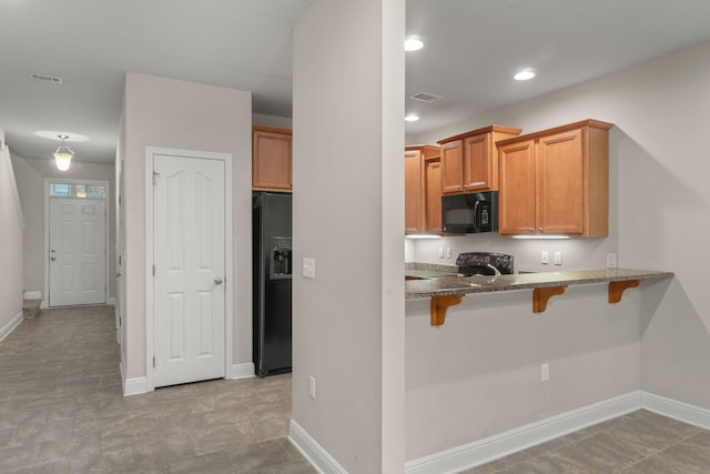 kitchen featuring black appliances, a breakfast bar, kitchen peninsula, and stone counters