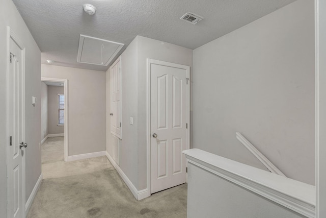 hallway with light colored carpet and a textured ceiling