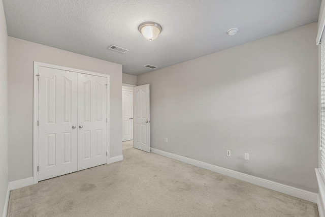 unfurnished bedroom featuring light colored carpet, a closet, and a textured ceiling