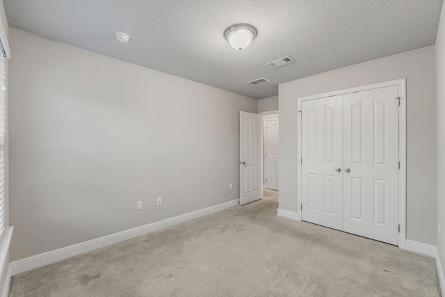 unfurnished bedroom featuring light colored carpet, a textured ceiling, and a closet