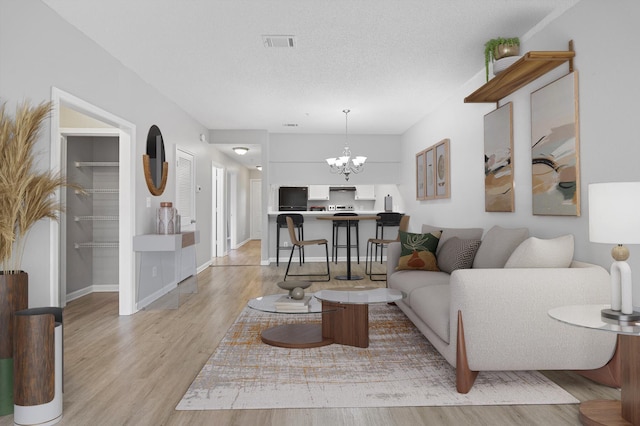 living room with a chandelier, a textured ceiling, and light wood-type flooring