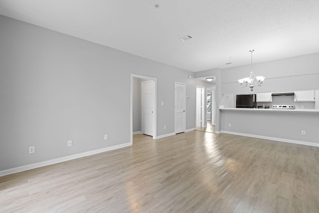 unfurnished living room featuring light hardwood / wood-style flooring, a textured ceiling, and a notable chandelier