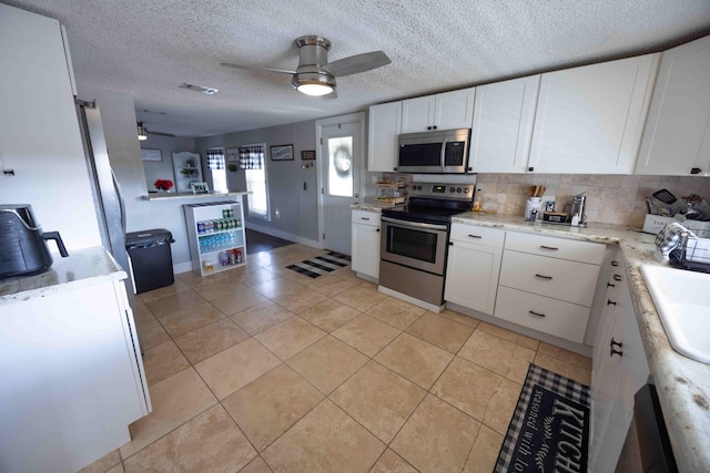 kitchen featuring a textured ceiling, stainless steel appliances, ceiling fan, sink, and white cabinetry