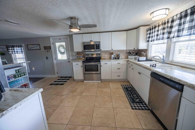 kitchen featuring sink, ceiling fan, light tile patterned floors, appliances with stainless steel finishes, and white cabinetry