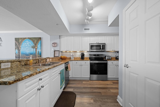 kitchen featuring kitchen peninsula, dark stone counters, stainless steel appliances, sink, and white cabinetry