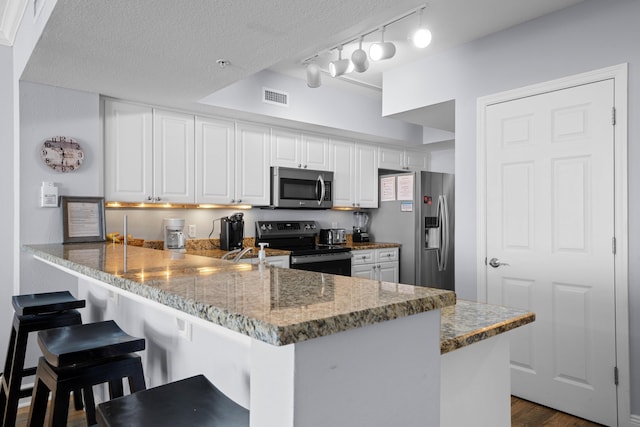 kitchen with kitchen peninsula, dark hardwood / wood-style flooring, a breakfast bar, stainless steel appliances, and white cabinets