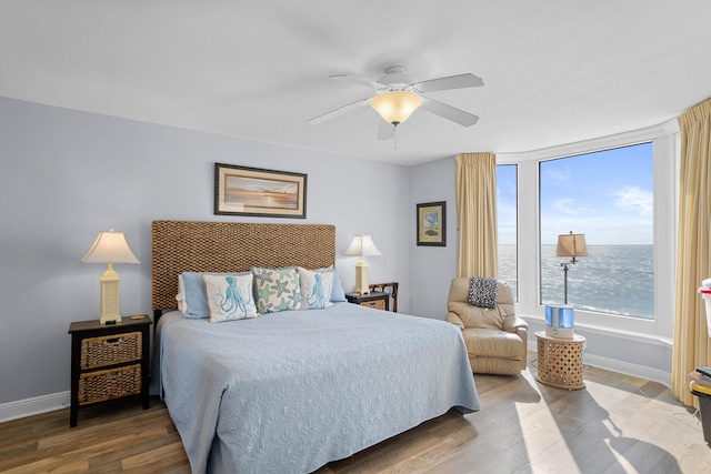 bedroom with hardwood / wood-style flooring, ceiling fan, and a water view