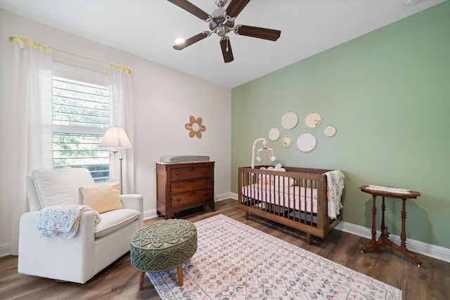 bedroom featuring ceiling fan, dark hardwood / wood-style flooring, and a nursery area