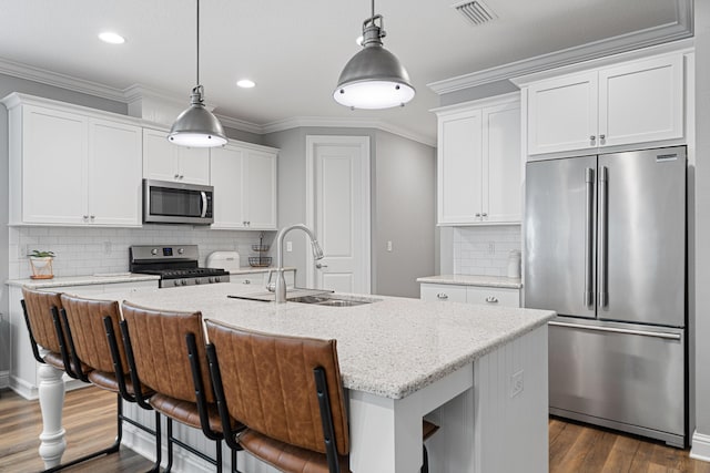 kitchen with sink, appliances with stainless steel finishes, pendant lighting, and an island with sink