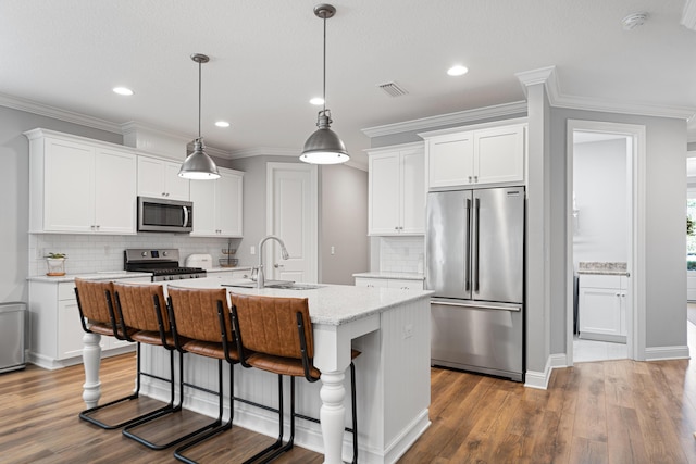 kitchen with decorative light fixtures, white cabinetry, stainless steel appliances, sink, and a center island with sink