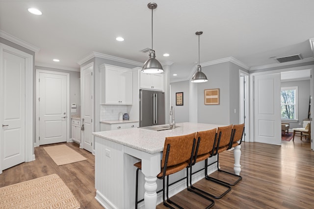 kitchen with high end refrigerator, a breakfast bar, hanging light fixtures, an island with sink, and white cabinets