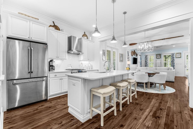 kitchen with sink, white cabinets, wall chimney exhaust hood, stainless steel fridge, and a center island with sink