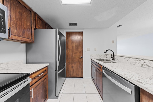 kitchen featuring light stone countertops, a textured ceiling, appliances with stainless steel finishes, light tile patterned flooring, and sink