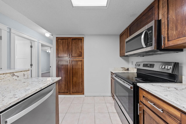 kitchen featuring stainless steel appliances, a textured ceiling, light tile patterned floors, and light stone counters