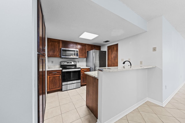 kitchen featuring kitchen peninsula, appliances with stainless steel finishes, light tile patterned flooring, and light stone countertops