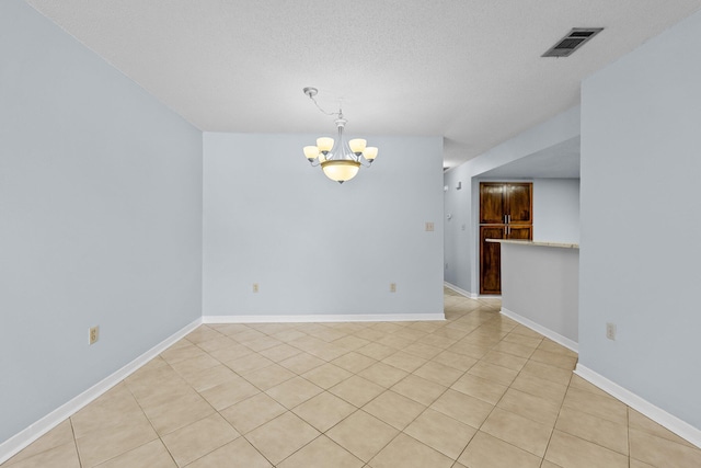 tiled empty room with a textured ceiling and an inviting chandelier