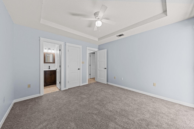 unfurnished bedroom with ceiling fan, ensuite bathroom, light carpet, and a tray ceiling