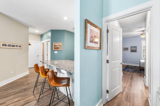 kitchen featuring a breakfast bar, ceiling fan, hardwood / wood-style floors, built in desk, and light stone countertops