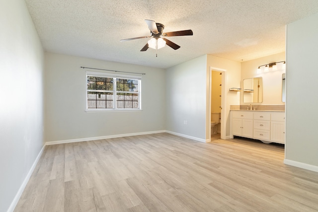 unfurnished bedroom featuring ensuite bathroom, ceiling fan, light hardwood / wood-style floors, and a textured ceiling